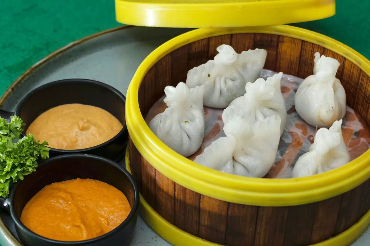 Steamed momo in a bamboo steamer with two chutneys