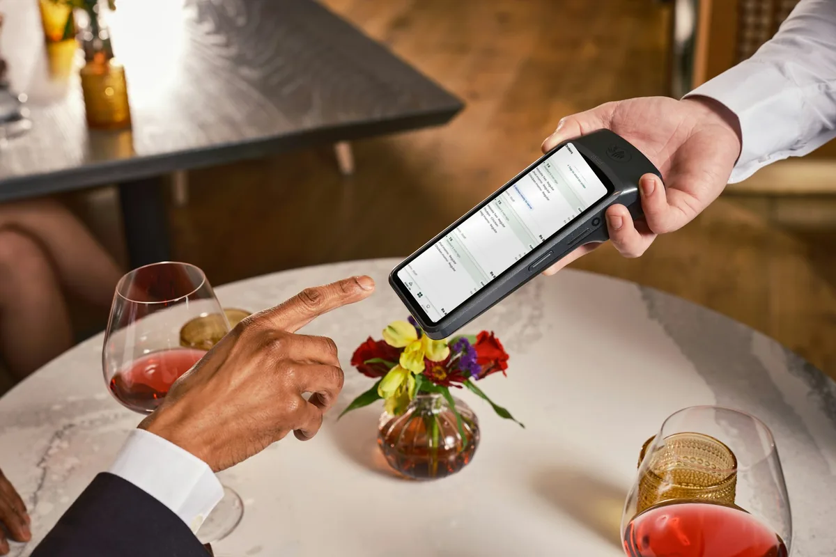 A waiter holding a handheld showing Cloudora Kitchen’s live table orders at a restaurant